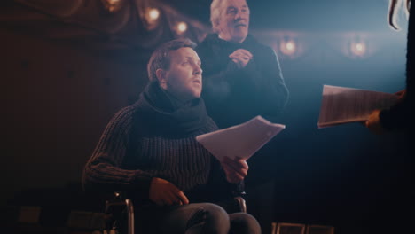 elderly director giving instructions to actors during rehearsal senior stage director giving instructions to man on wheelchair then watching actors acting out quarrel scene during rehearsal in theater