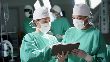 diverse female surgeons using tablet in operating theatre at hospital, slow motion