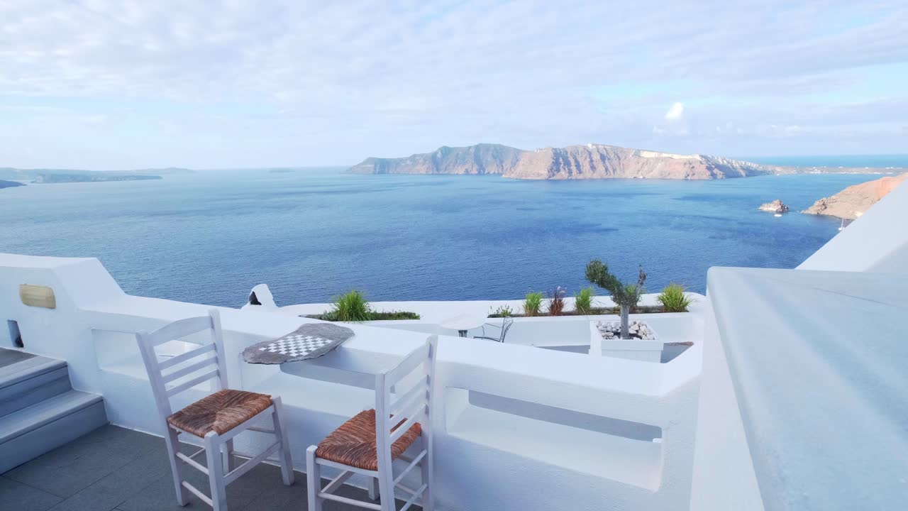 dos sillas blancas con ajedrez en un balcón con vista a la caldera en oia, santorini