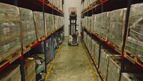 unrecognizable worker driving forklift between tall shelves of warehouse