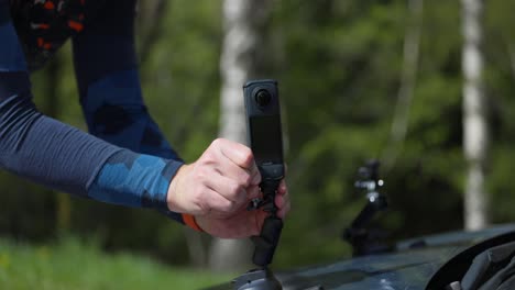 las manos de un hombre asegurando el insta360 x4 al capó de un coche - primer plano