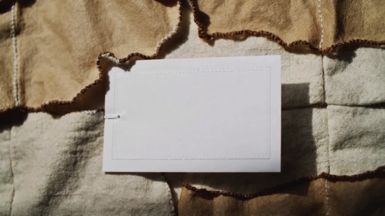 Una carta bianca su una trapunta mentre la luce mutevole proietta una debole ombra, con un bordo in rilievo e un foro perforato.
