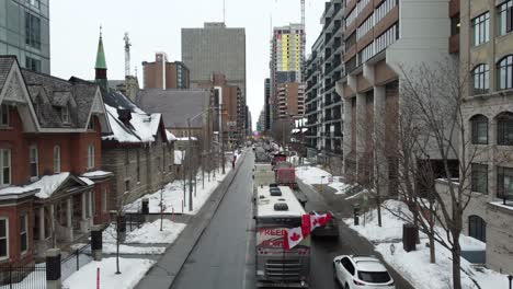 canadian flags fluttering in the wind and multiple trucks blocking a road in the parly with snow covered downtown of ottawa as being part of the freedom convoy in canada