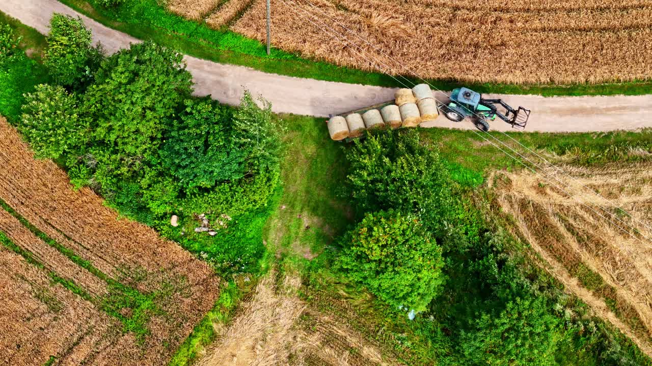 Aerial view of tractor hauling hay bales near field and dirt road in countryside