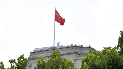 chinese flag fluttering in the wind on top of a building in the city of shanghai, slowmotion