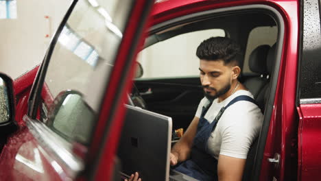 mecánico usando una computadora portátil para diagnosticar un coche rojo