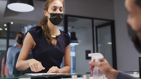 Una-Mujer-Caucásica-Con-Mascarilla-Tiene-Las-Manos-Desinfectadas-Por-Un-Colega-Masculino-En-El-Mostrador-De-Recepción-De-La-Oficina