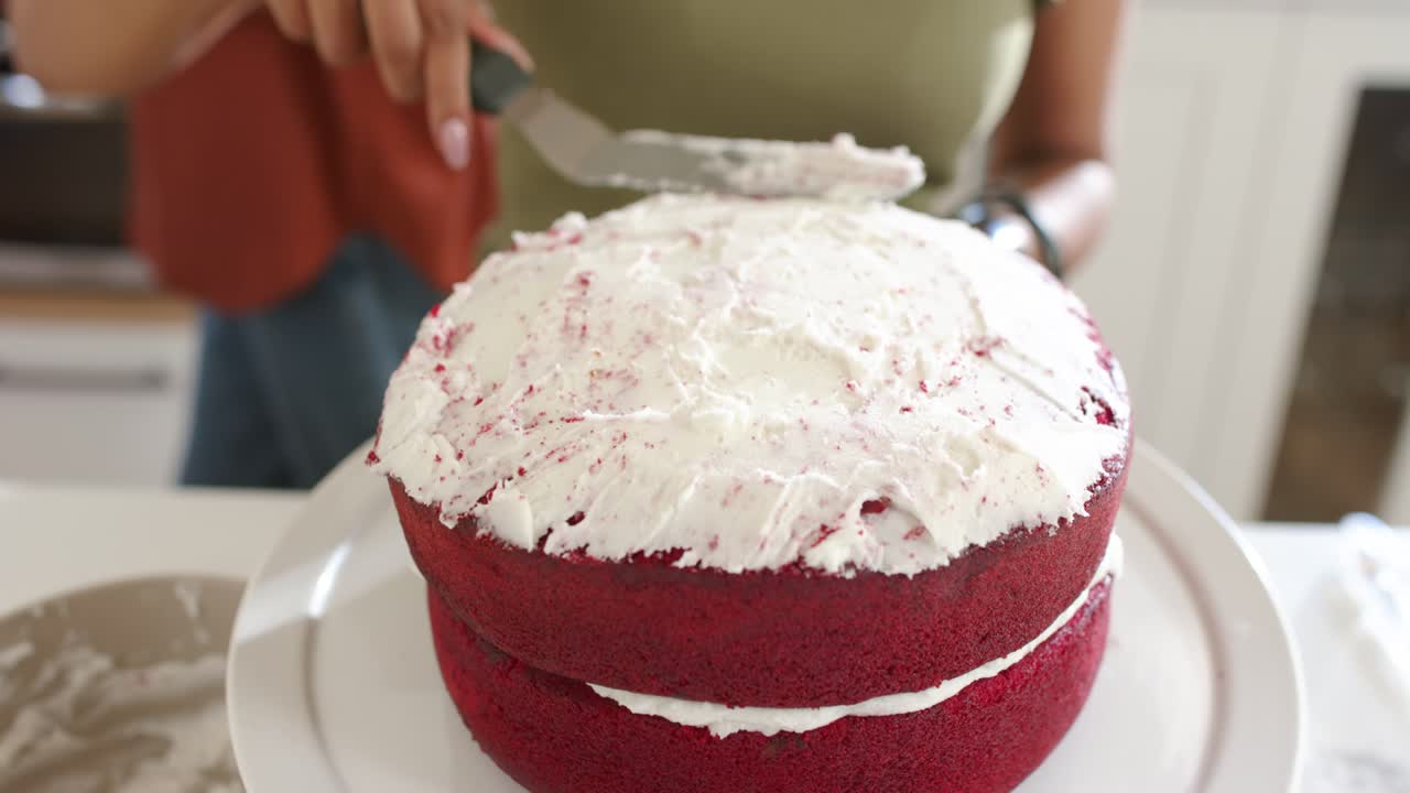 Placing offset spatula, home baker is smoothing frosting on rotating plate in kitchen to even top