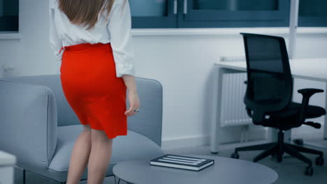 Beautiful-young-woman-with-dark-hair-sitting-on-a-grey-couch-in-office-and-flipping-pages-of-a-designer-book