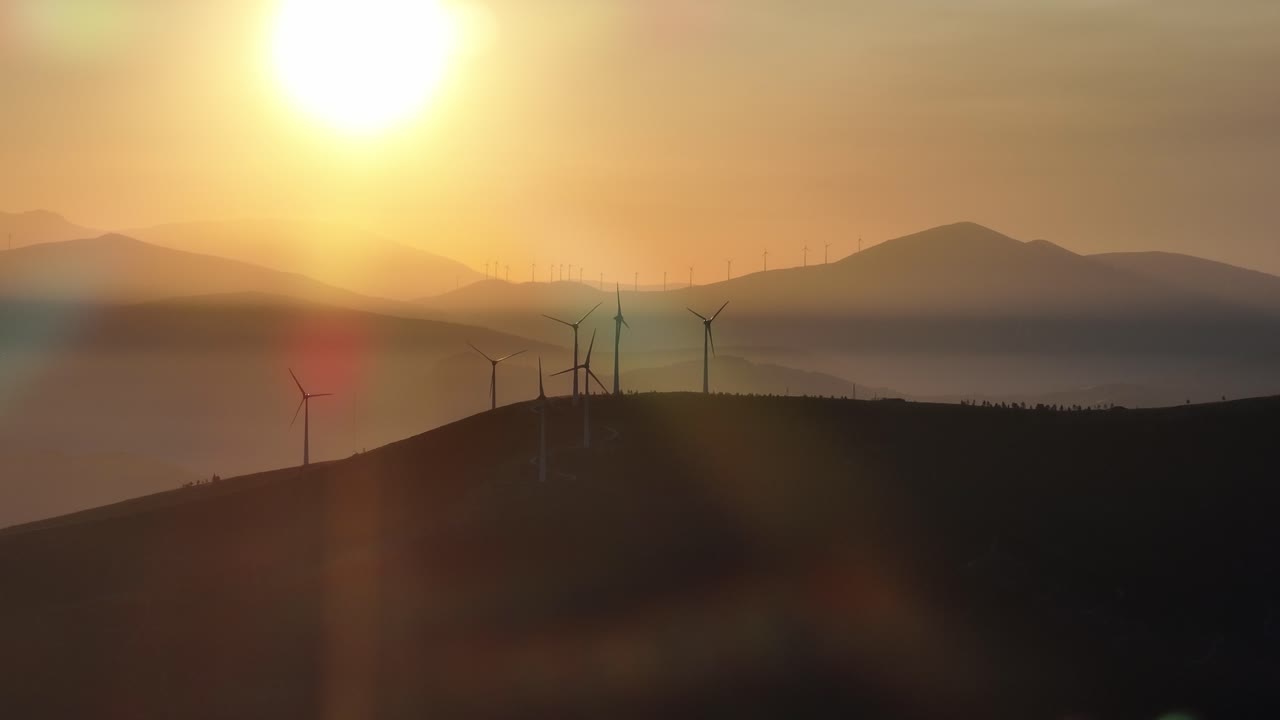 Slowly moving drone footage of wind turbines slowly rotating at sunrise.