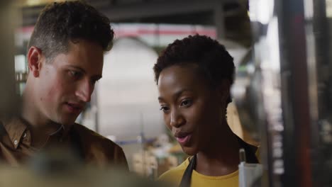 Diverse-male-and-female-colleague-at-gin-distillery-inspecting-equipment-and-discussing