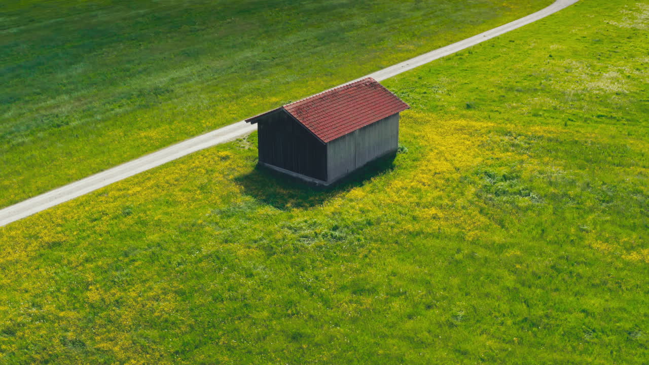 Dronebillede af et træskur til landbrugsudstyr ved siden af en landevej omgivet af marker