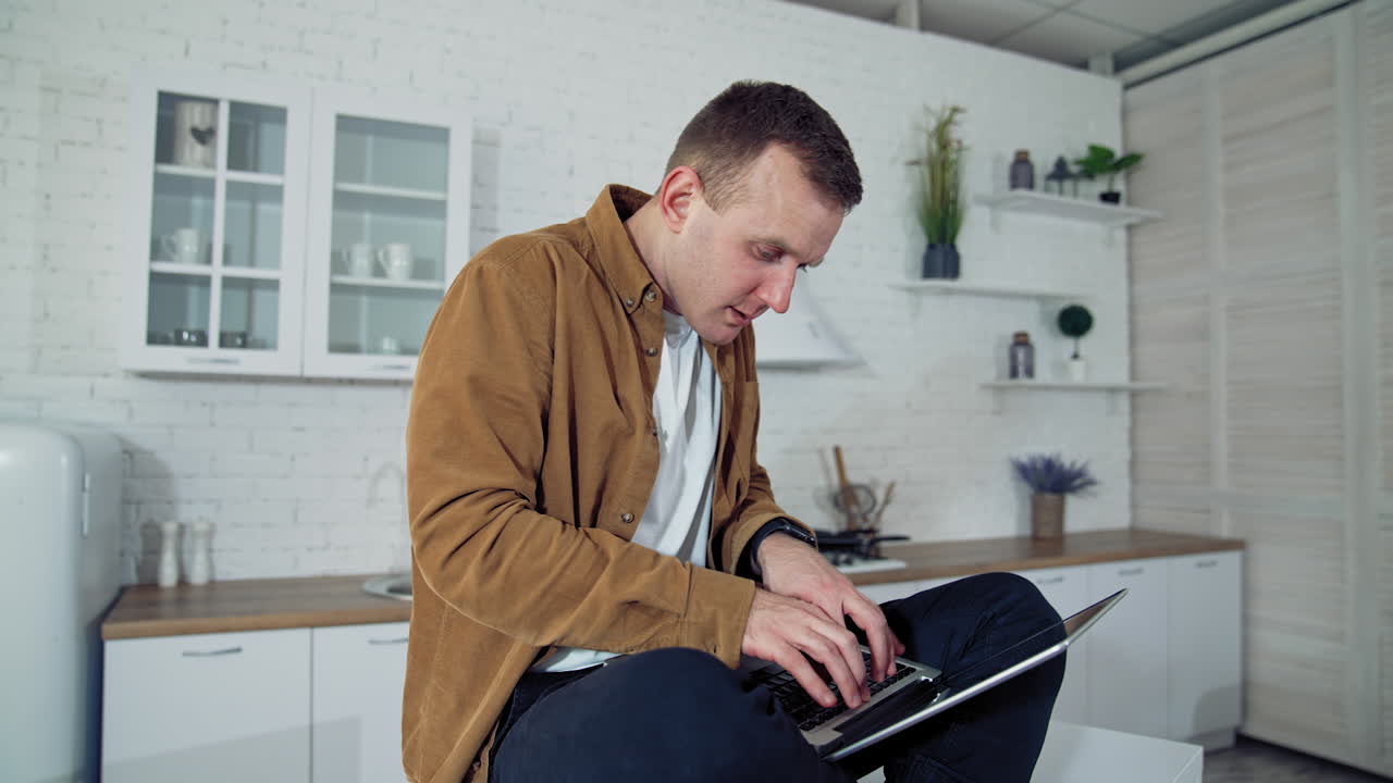 Oddball man with a laptop. Funny man sitting on a table and typing the laptop looking to the sides during long quarantine process. Consequences of pandemic.