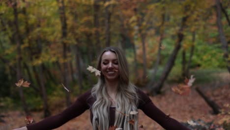 beautiful blonde young woman tossing fall autumnal color leaves in the air