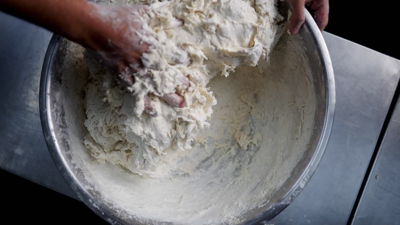 Top view of hands kneading and mixing flour in a bowl in a restaurant kitchen in slow motion.
