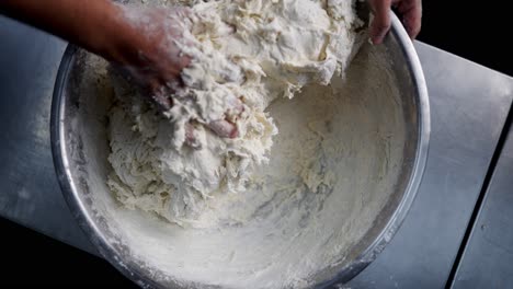 top view of hands kneading and mixing flour in a bowl in a restaurant kitchen in slow motion.