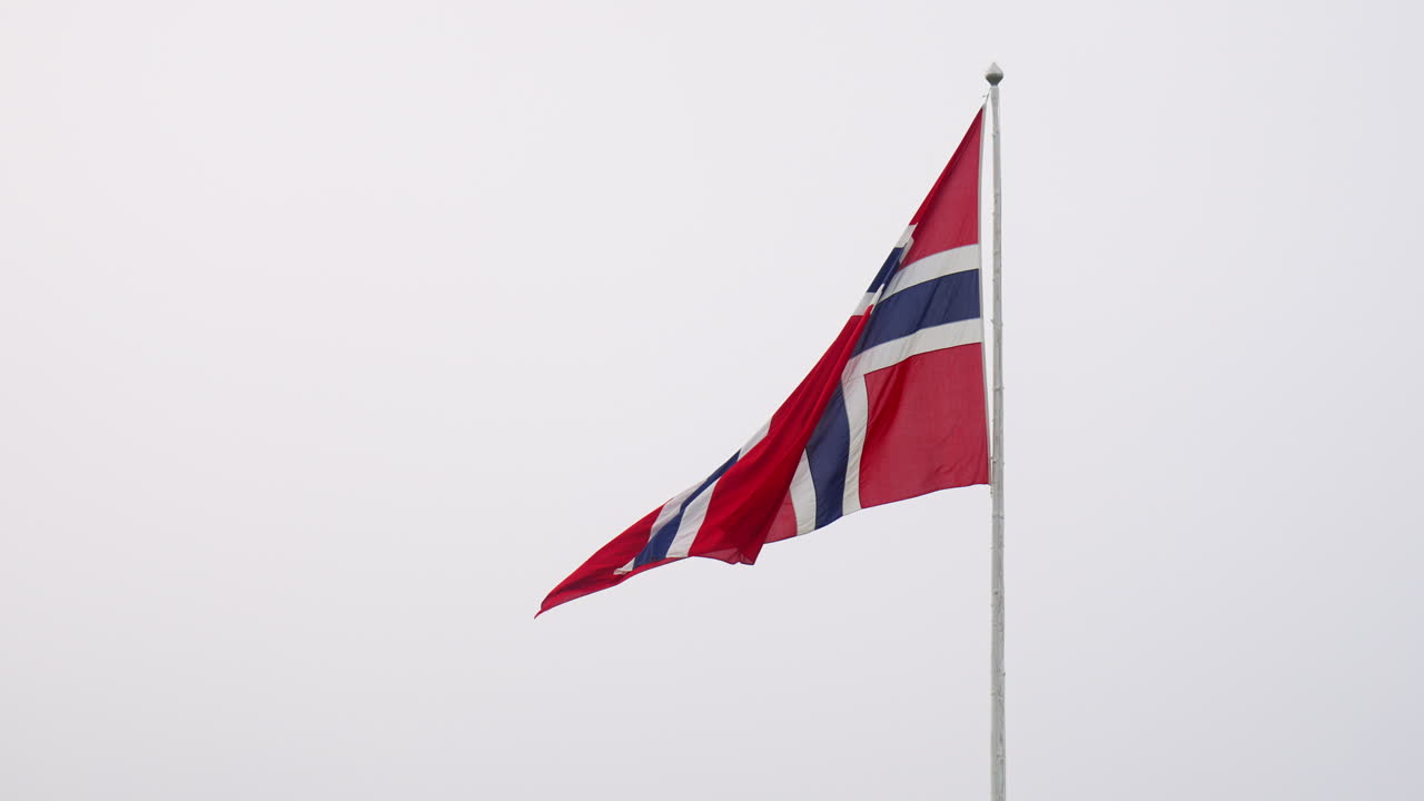 Norwegian flag ripples slowly against a bright white sky Close up