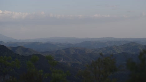a serene, long-range view of layered mountain ridges fading into the horizon under a soft blue sky. the low light of dusk enhances the dimensional contrast between the ranges.