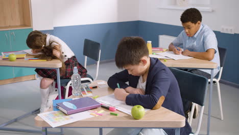 group of multiethnic primary pupils writing in their notebook during english class at school