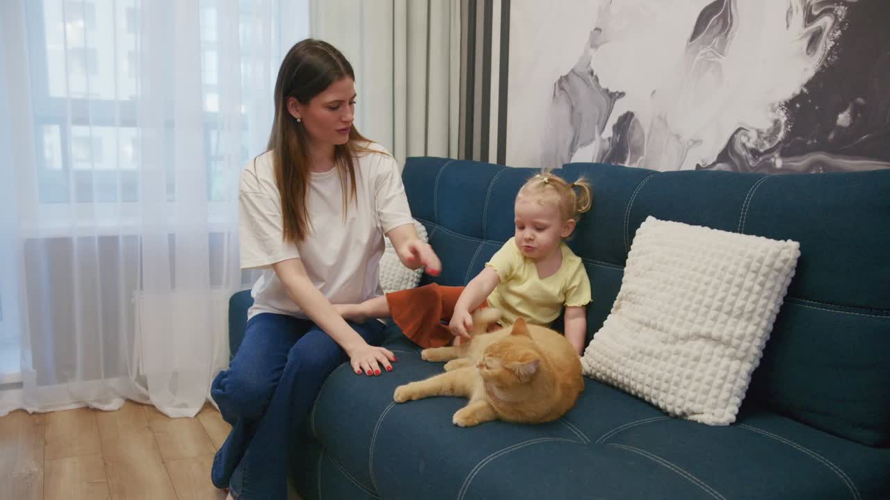 Mor og småbarnsdatter som klapper en rød katt i en sofa