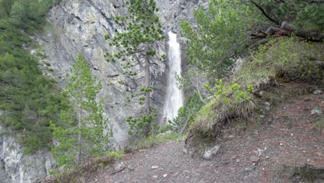 Aerial-drone-shot-rolling-slowly-to-the-left-to-reveal-a-dramatic-waterfall-cascading-over-the-edge-of-a-sheer-mountain-cliff-in-Switzerland-surrounded-by-pine-trees