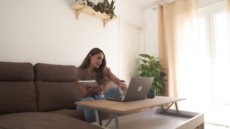 happy woman writing in diary while working on laptop at home