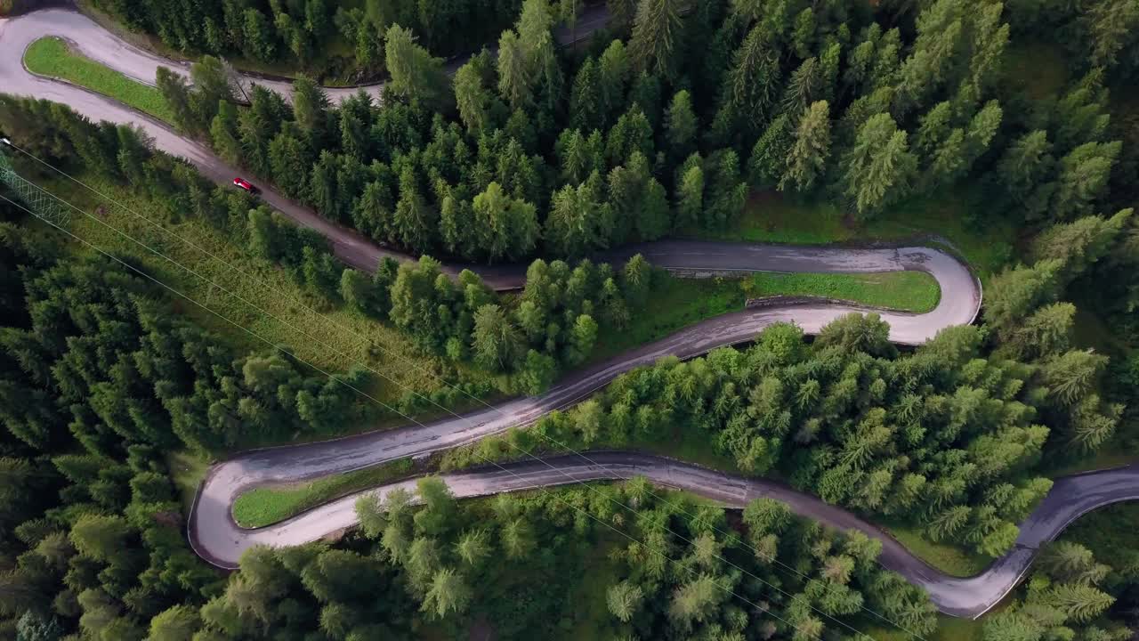 camino sinuoso con coche rojo subiendo la montaña en la zona de dolomita del norte de italia, tiro giratorio de la vista aérea de drones