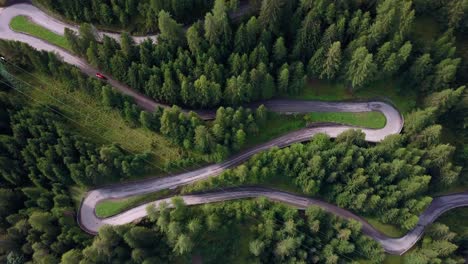 Kurvenreiche-Straße-Mit-Rotem-Auto,-Das-Den-Berg-In-Der-Dolomitregion-Norditaliens-Hinauffährt,-Rotierende-Aufnahme-Aus-Der-Luftdrohne-Von-Oben