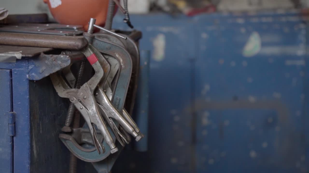 Slow panning shot showing metal clamps and locking pliers hanging from blue workbench in industrial workshop