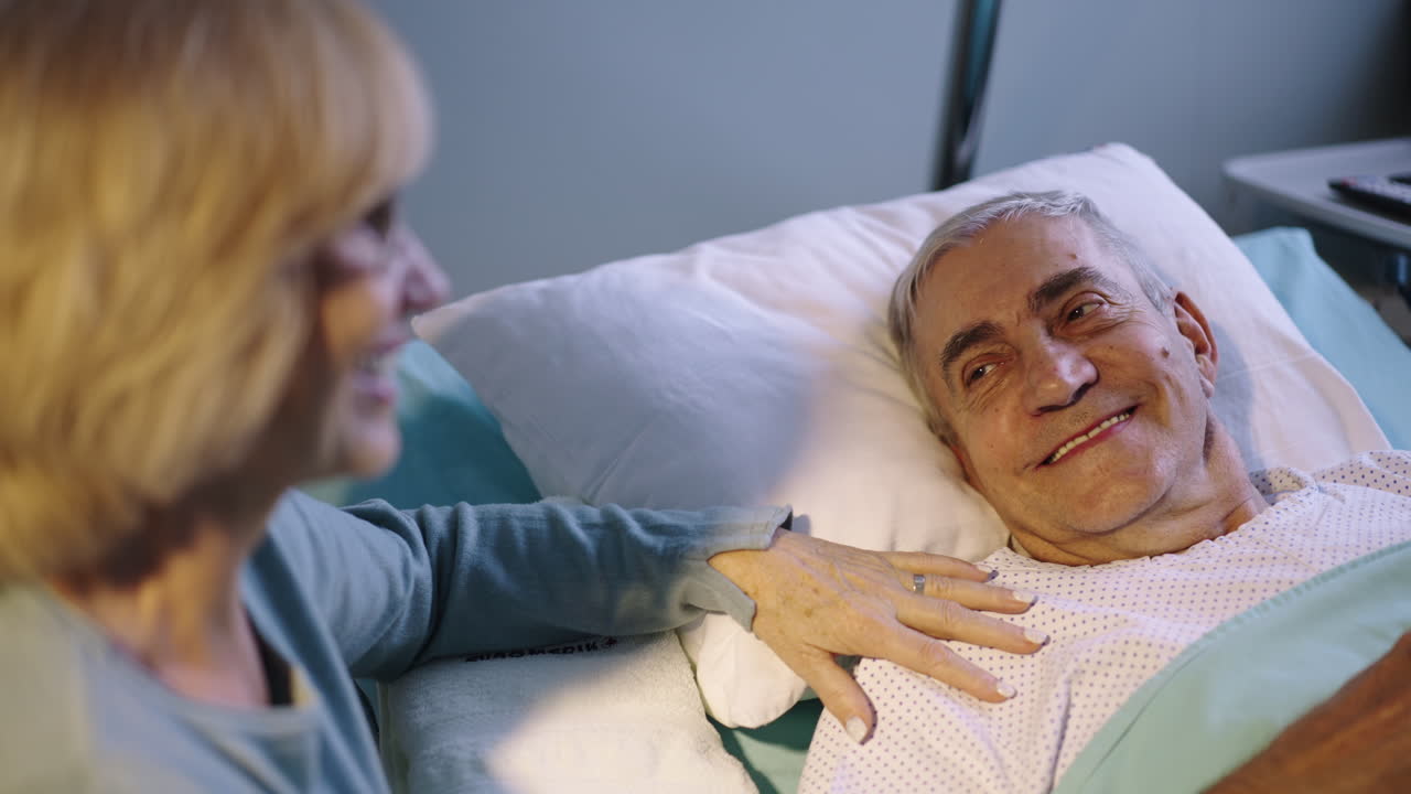 Elderly man in hospital bed with visiting woman