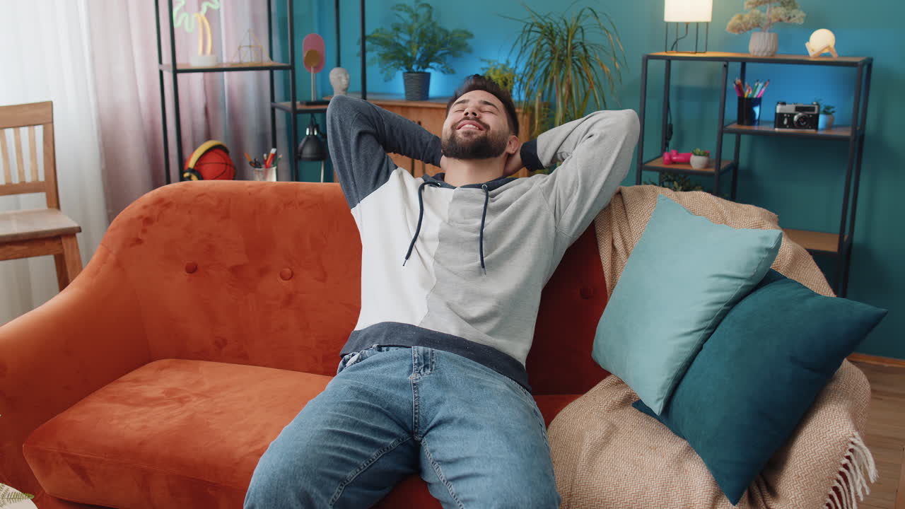 Tired young man lying down on comfortable couch taking a rest daytime nap relaxing falling asleep