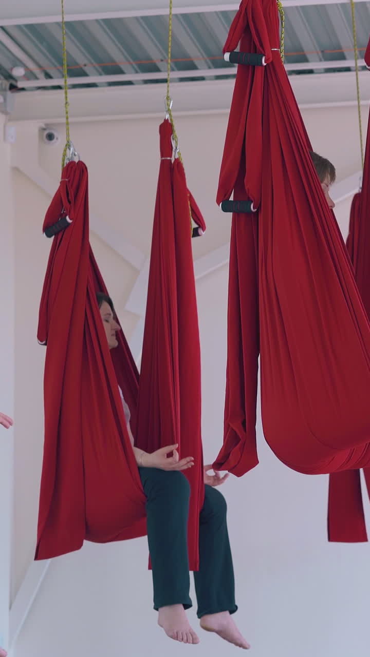 concentrated ladies hold fingers in gyan mudra position and practice relaxing butterfly asana sitting in hammocks