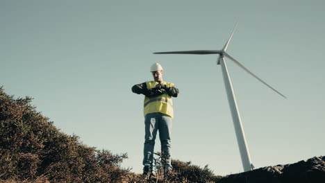 a professional caucasian engineer in a reflective vest and helmet checks wind turbines in a field, showcasing the dedication to sustainable energy production