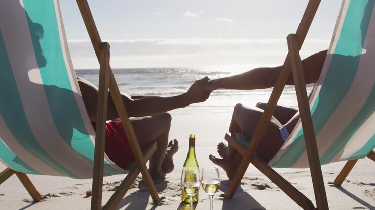 Couple afro-américain se tenant la main, assis sur des chaises longues à la plage