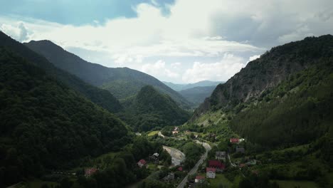 Aerial-drone-shot-of-village-houses-in-the-valley-surrounded-by-mountain-range-on-all-sides-in-Lepsa,-Romania-on-a-cloudy-day