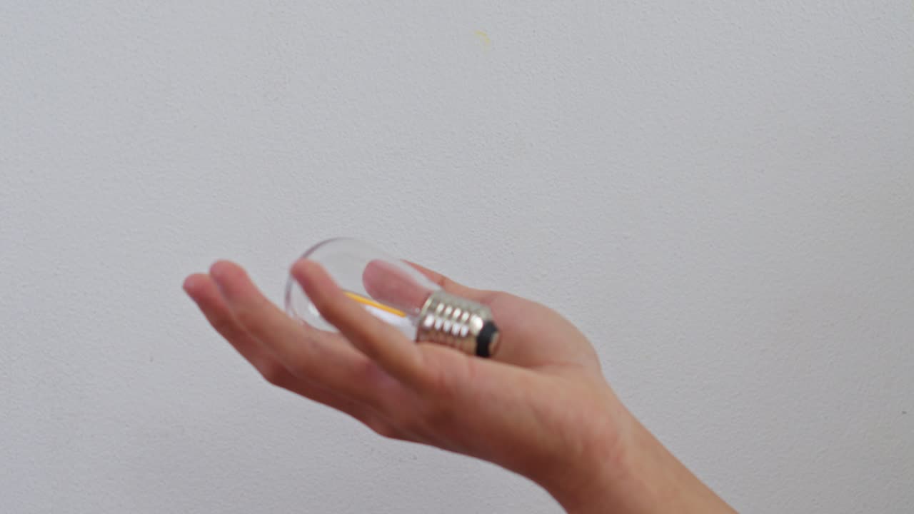 Hand holding clear LED light bulb against white wall