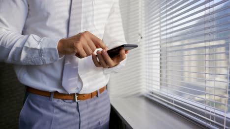 Mid-section-of-young-Caucasian-male-executive-using-mobile-phone-near-window-in-modern-office-4k