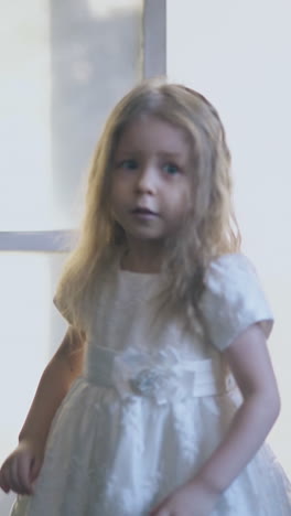 pretty little blond girl in festive dress with bow opens large forged lattices of room entrance in foggy background