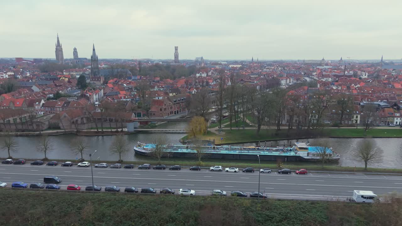 Un drone laterale segue una barca che si muove lungo i canali di Bruges, rivelando l'architettura storica medievale, il paesaggio fluviale e il fascino di questa città belga