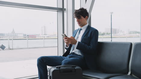 businessman sitting in airport departure lounge using mobile phone