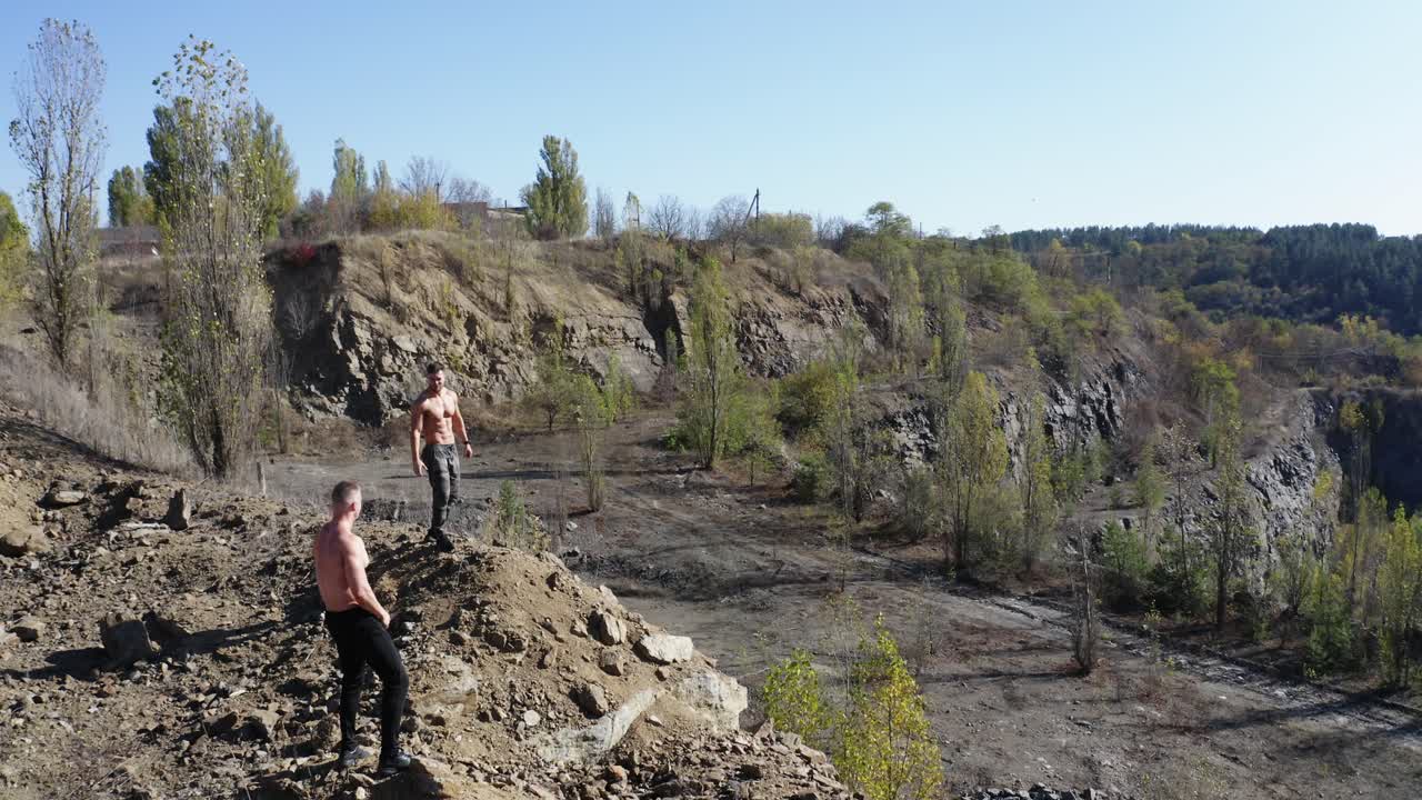 Sporty men with muscular body on the rocky hills. Two athletic guys without shirt having workout on the beautiful nature background in summer. Aerial view.