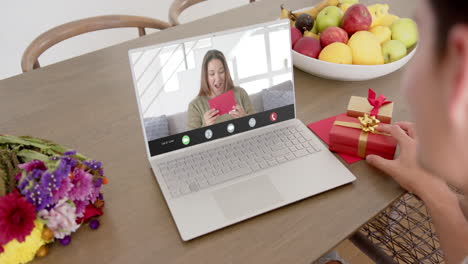 Caucasian-woman-holding-gift-and-talking-with-caucaslan-woman-on-laptop-screen