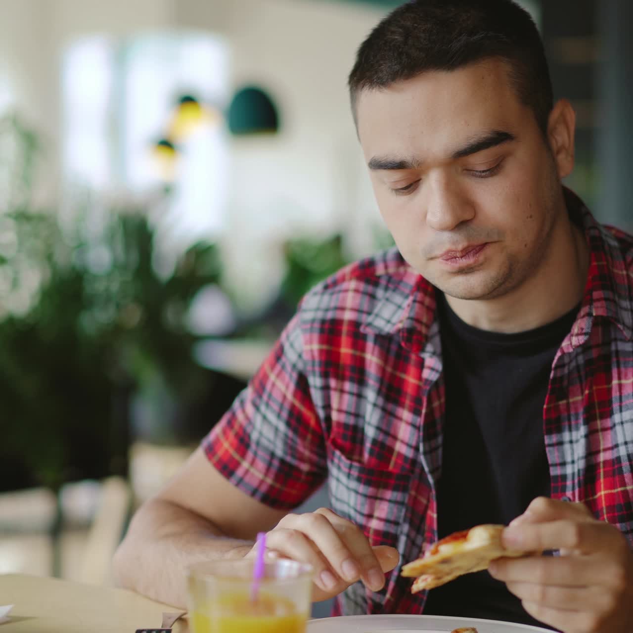handsome man in a plaid shirt is eating pizza at a cafe for lunch on a blurred background. Pizzeria