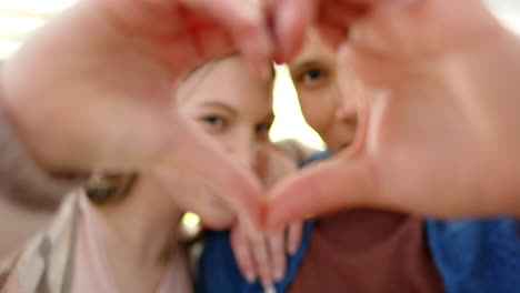 retrato de una feliz pareja diversa haciendo forma de corazón con las manos en un jardín soleado, en cámara lenta