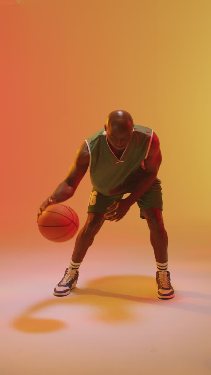 Turuncu arka planda top sektiren Afrikalı Amerikalı erkek basketbolcunun dikey videosu