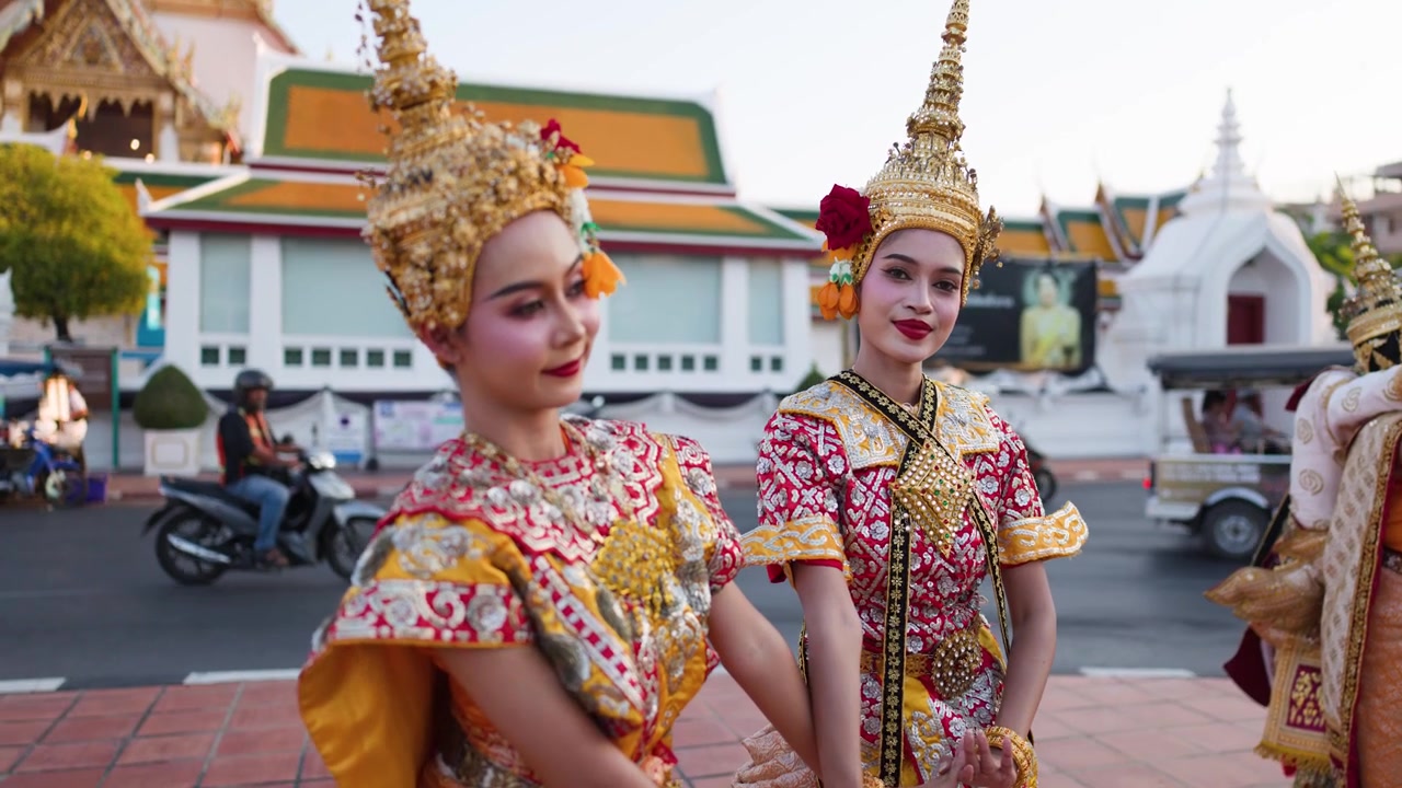 Dançarinos tailandeses em trajes dourados ornamentados realizam movimentos tradicionais do lado de fora de um templo histórico de Bangkok.