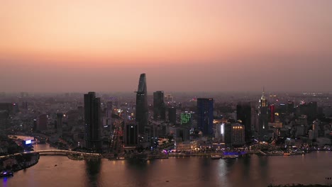 Ho-Chi-Minh-City,-Vietnam-iconic-Skyline-and-Saigon-river-waterfront-aerial-panorama-on-a-busy-evening-featuring-key-buildings-illuminated-against-beautiful-colored-sky-and-reflected-in-the-river