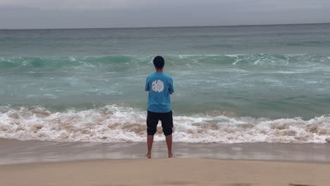 back view of an indian man standing on the beach while looking to the ocean