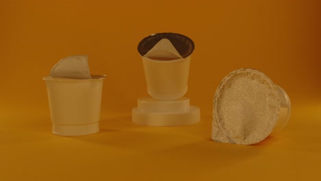 production samples of plastic yogurt cups with aluminum lids on the orange background with a light sweep