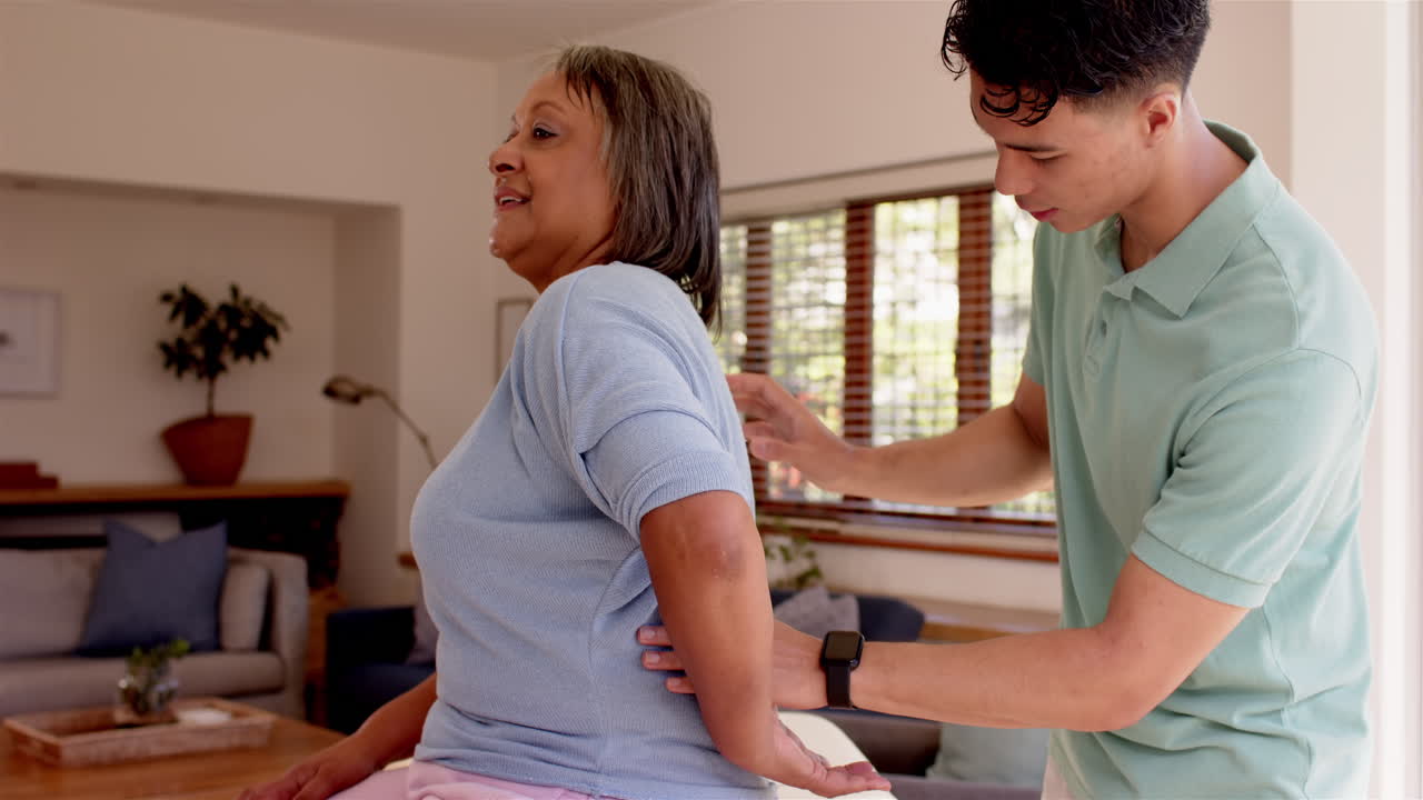 Physiotherapist assisting senior woman with back exercises in living room
